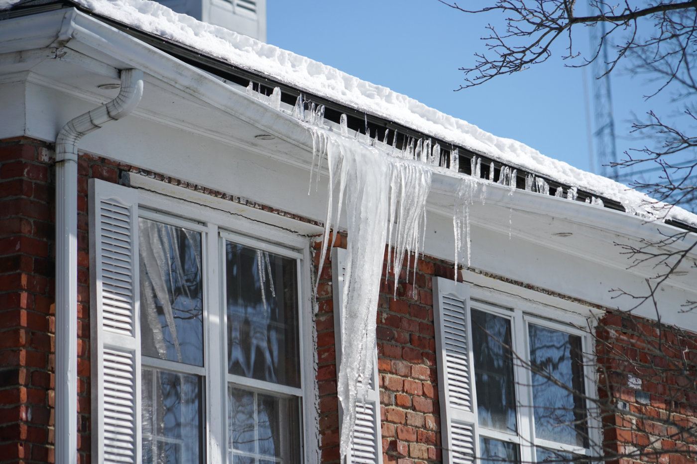 Eavestrough gutter ice dam build up destroying residential roof in winter.