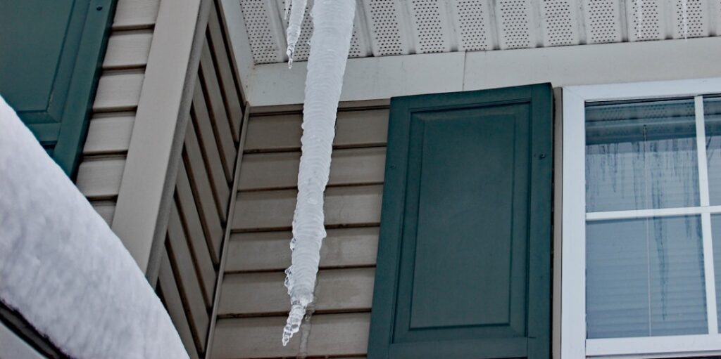 Snow on roof and Icicle hanging from an eavestrough from winter ice dam build-up.