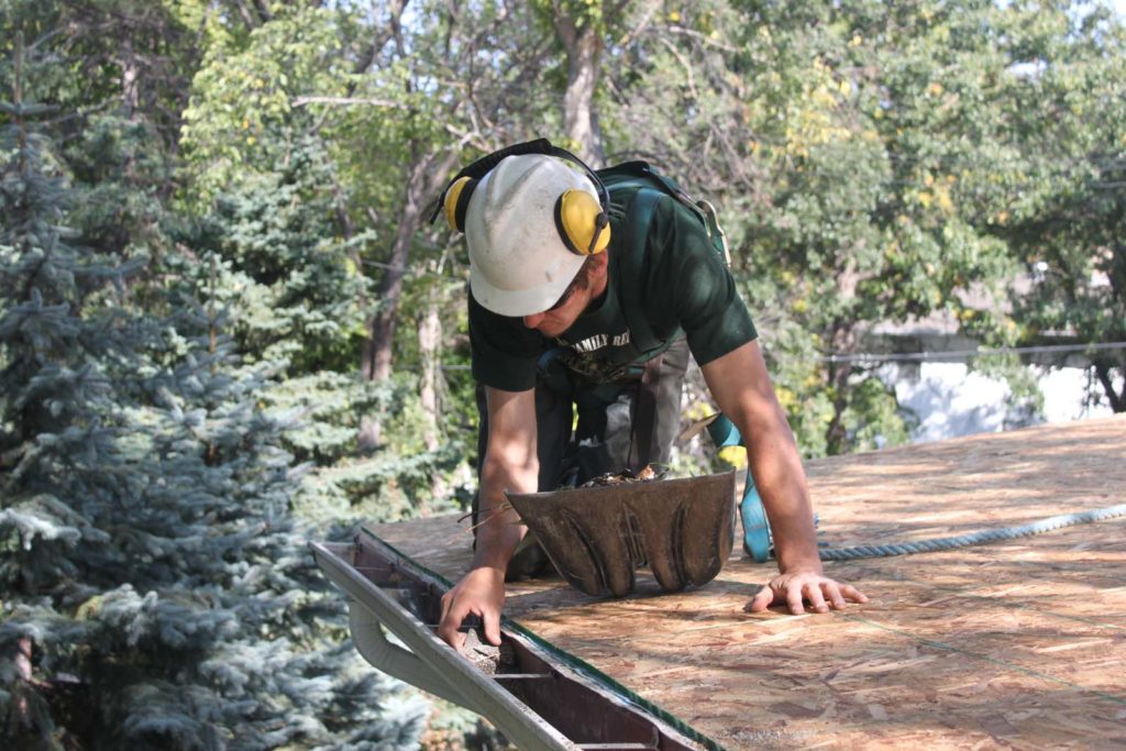 Worker cleaning debris from eavestrough. Benefits of Installing New Eavestroughs.