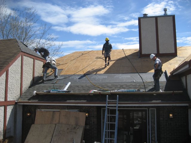 Three roofers installing new shingles to a small home.