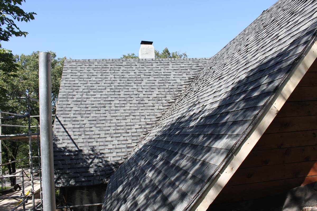 A grey asphalt shingle roof with a chimney and a dormer on a partially constructed home.