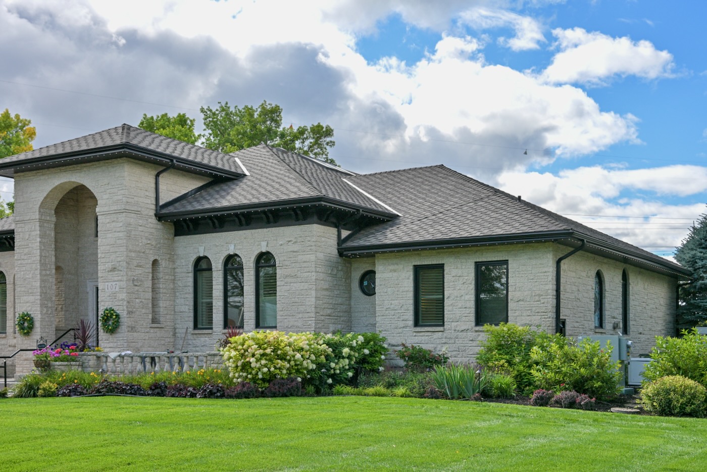Modern stone house with dark shingle roof and landscaped front yard.