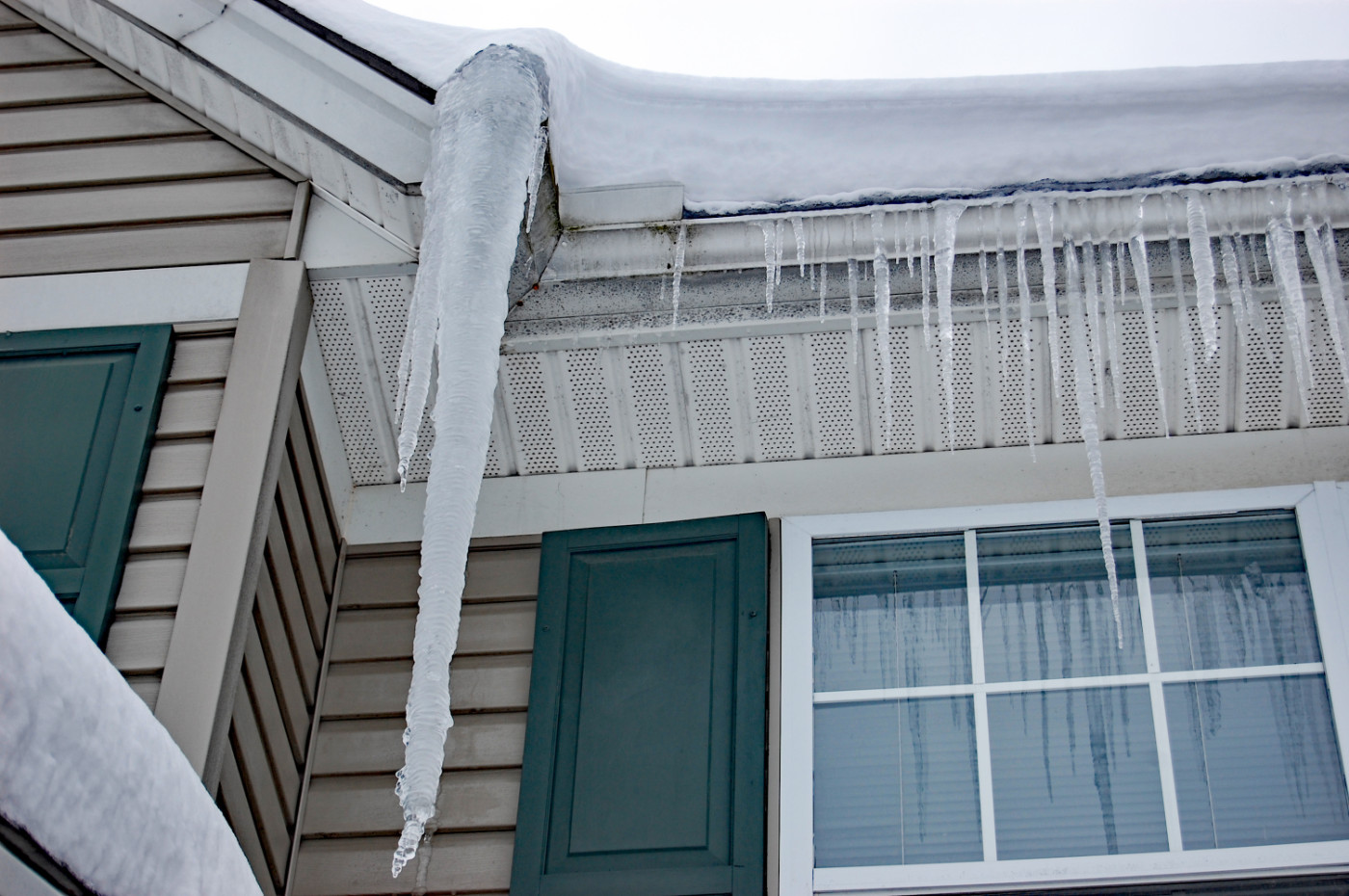 Snow on roof and Icicle hanging from an eavestrough from winter ice dam build-up.
