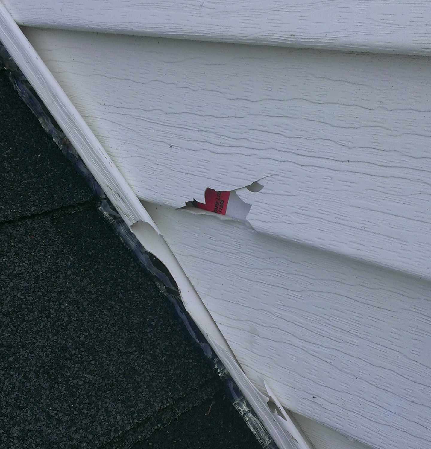 Cracked siding panel exposing underlayer above shingles
