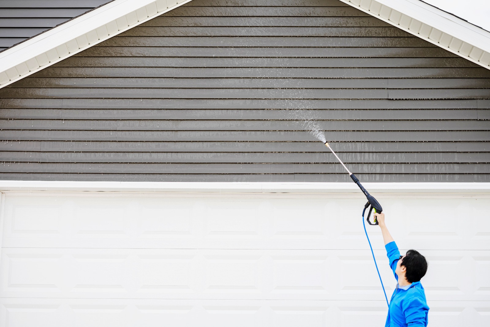 Homeowner power washing and maintaining vinyl siding exterior.
