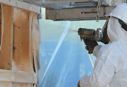 Worker in protective gear spraying foam insulation.