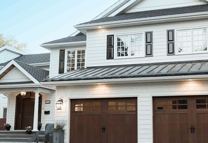 White house with wooden garage doors and metal roof.