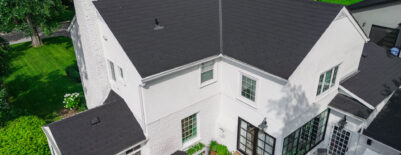 White brick house with black shingle roof and backyard deck with seating.