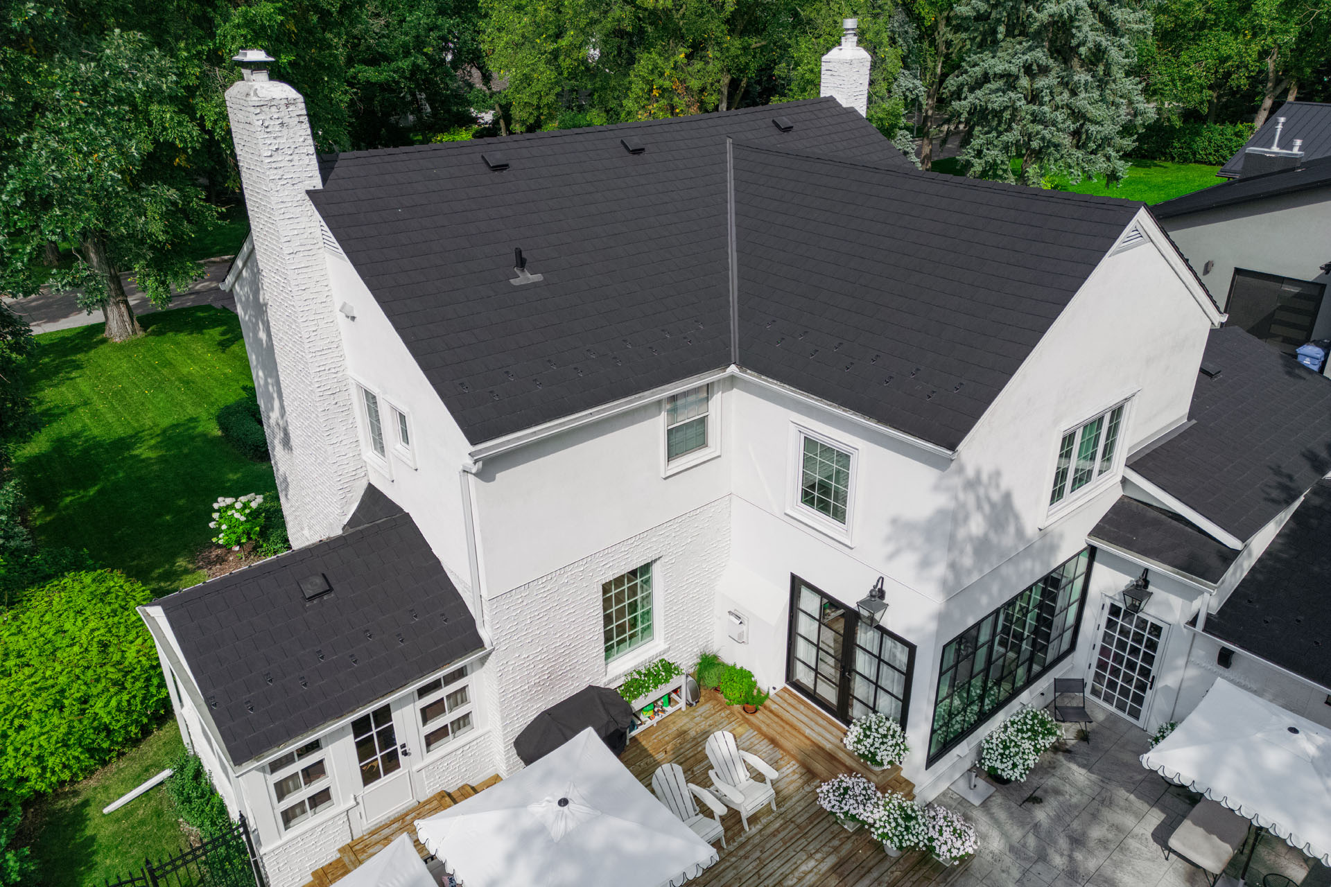White brick house with black shingle roof and backyard deck with seating.