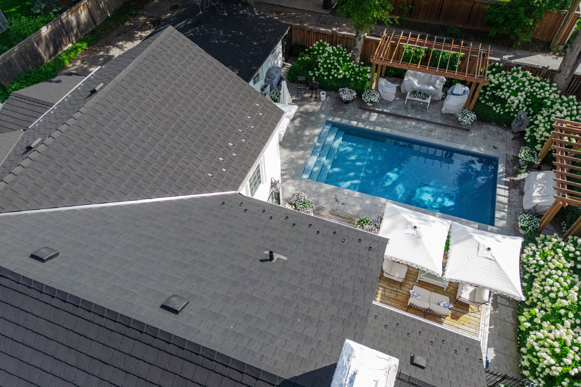 Aerial view of home with black shingle roof and backyard pool with patio.