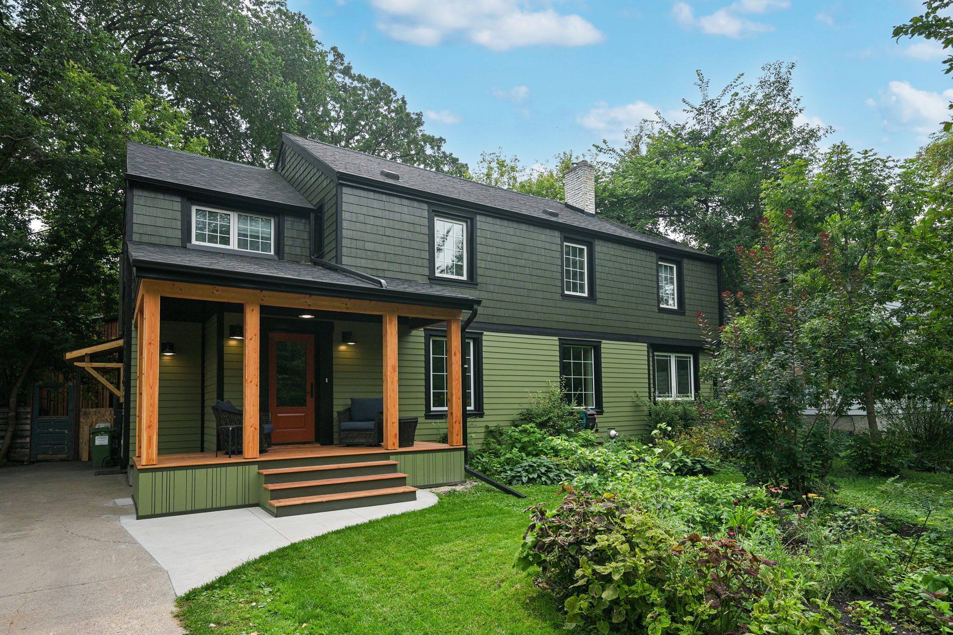 Green siding two-story house with black shingle roof and front porch.