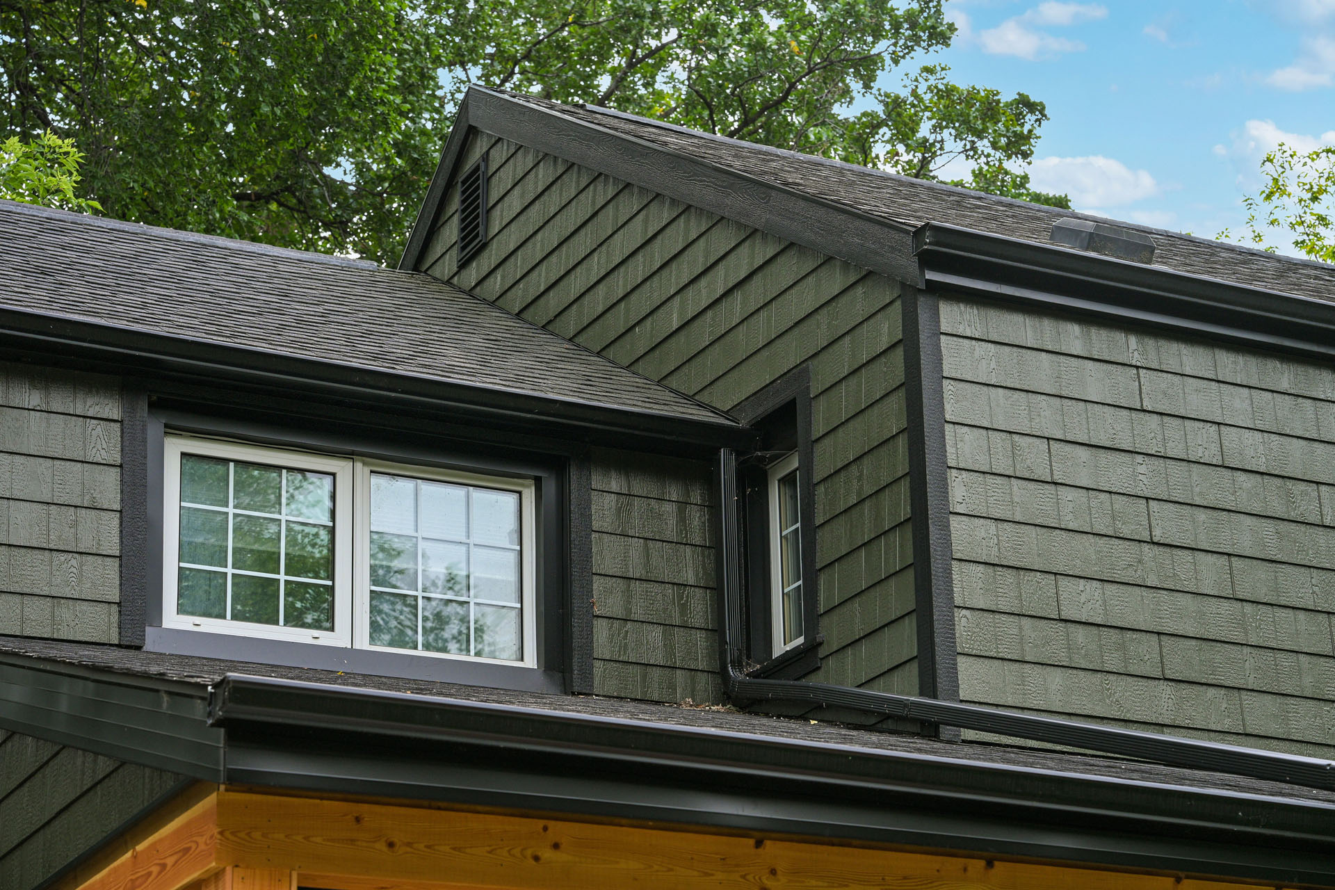 Close-up of green siding house with black shingle roof and window trim.