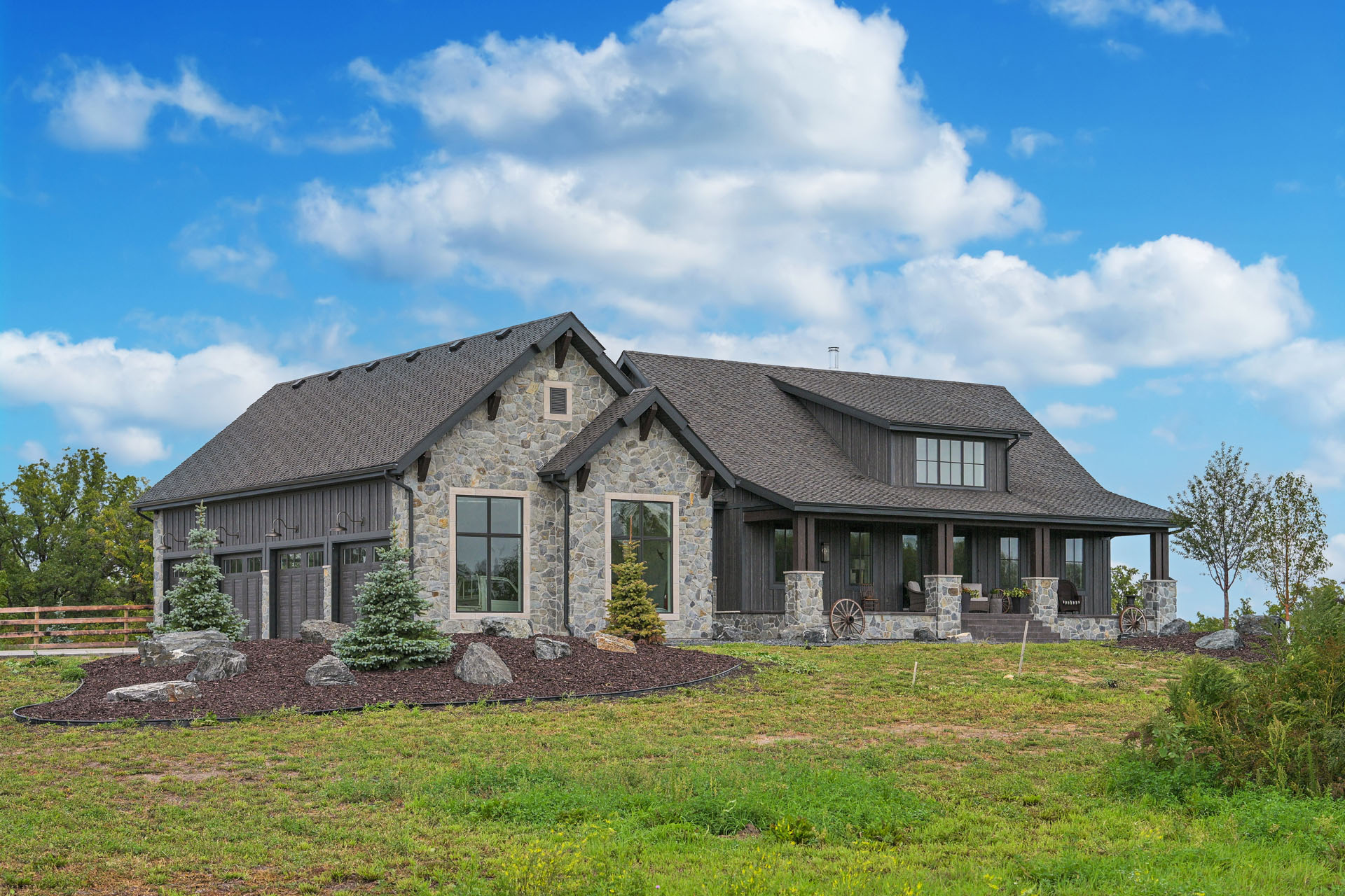 Stone and wood house with dark shingle roof and covered front porch.