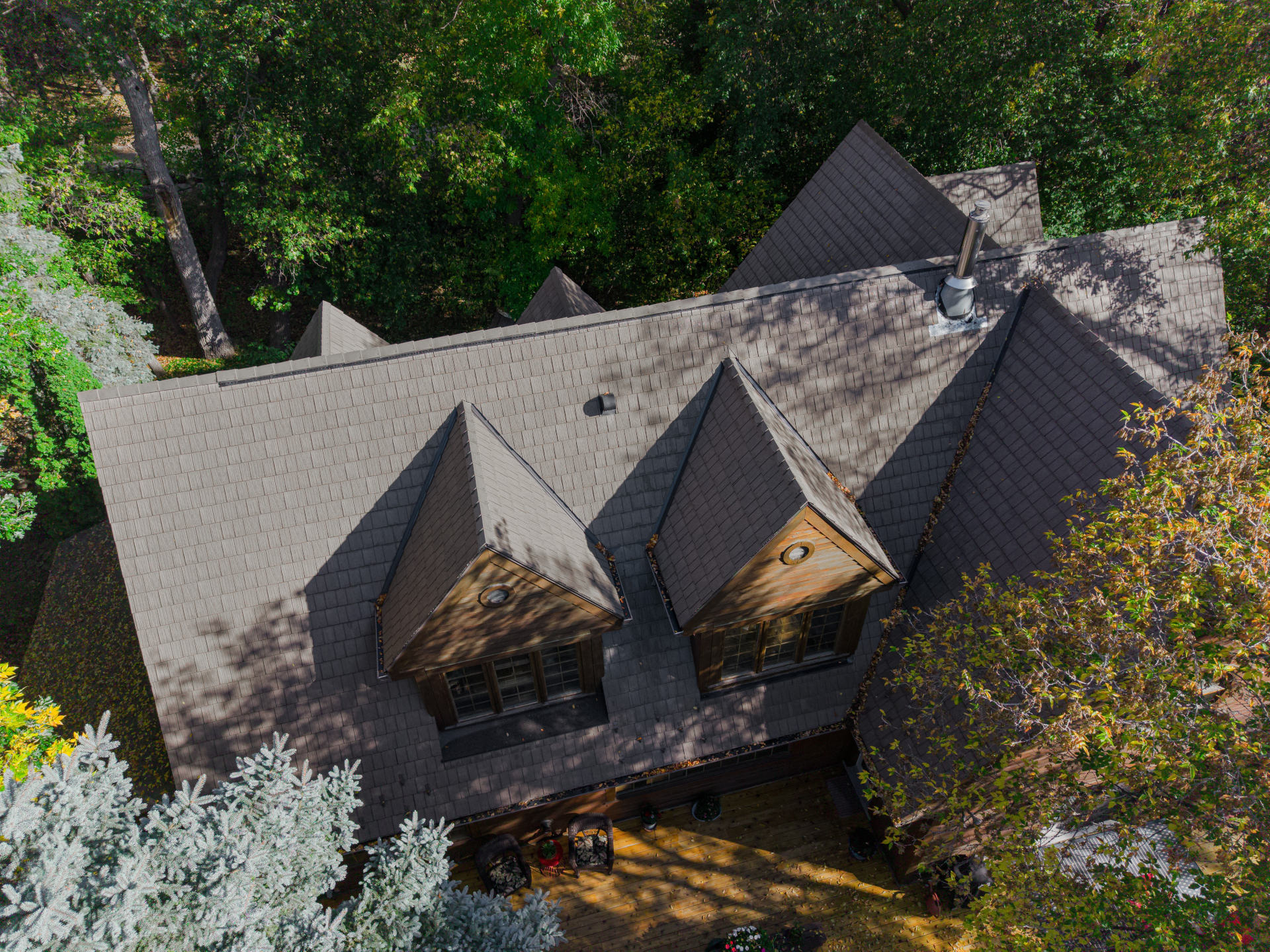 Aerial view of steep shingle roof with dormers surrounded by dense trees.